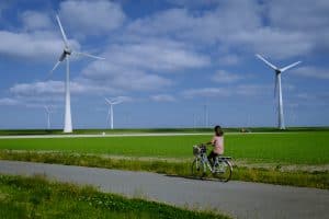 young woman electric green bike bicycle by windmill farm, windmills isolated on a beautiful bright day Netherlands Flevoland Noordoostpolder Holland